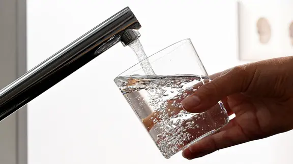 Wasser läuft aus einem Hahn in ein Glas.