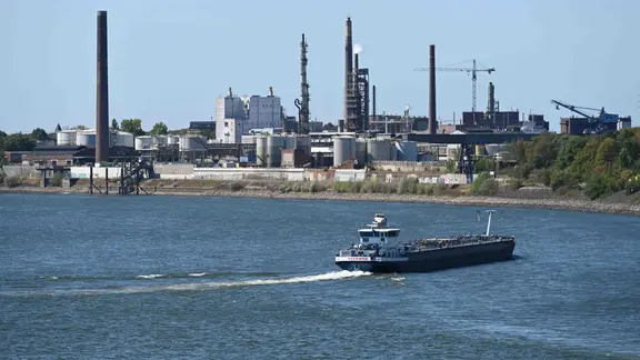 Frachtschiffe fahren auf dem Rhein bei Duisburg-Ruhrort, im Hintergrund ist die industrielle Skyline mit der Chemieindustrie zu sehen. Duisburg-Homberg in Duisburg, 11.08.2026.