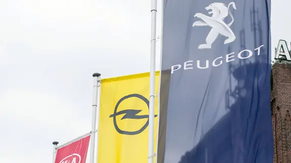Fahnen von Peugeot, Opel und Kia vor einem Autohaus.