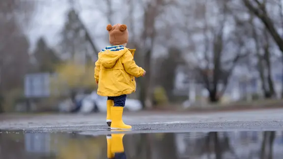 Ein kleiner Junge trägt Gummistiefel und eine Regenjacke.