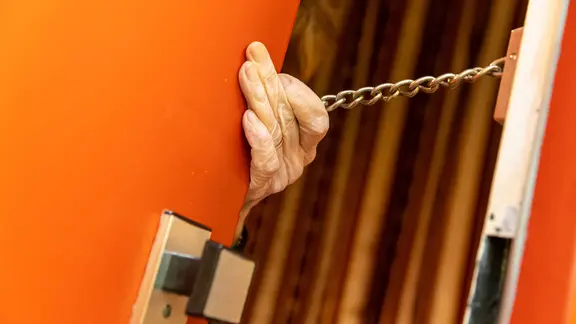 Eine Seniorin hält die Kette ihrer geöffneten Wohnungstür