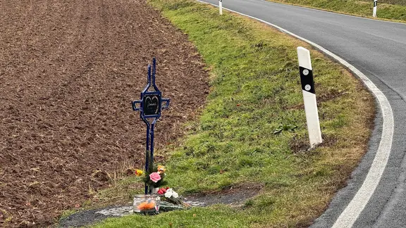 Ein Unfallkreuz steht im Straßengraben einer Landstraße