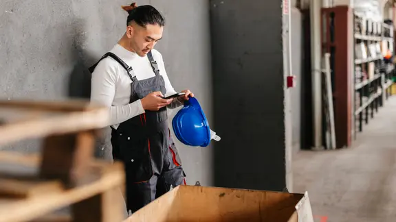 Ein Fabrikarbeiter benutzt sein Smartphone in einer Arbeitspause.