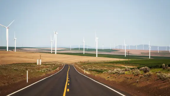 relativ gerade, typische amerikanische Landstraße, links und rechts Grasland und Felder, viele Windräder bis zum Horizont, warme natürliche Farben