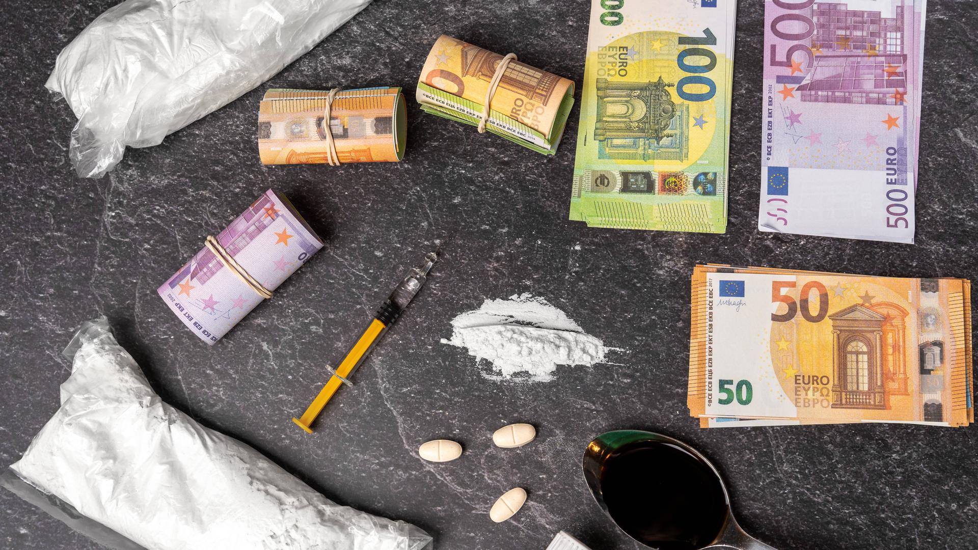 Drogen, Spritze, Tabletten und Geldscheine liegen nebeneinander und zeigen den illegalen Drogenhandel.  | IMAGO / Bihlmayerfotografie