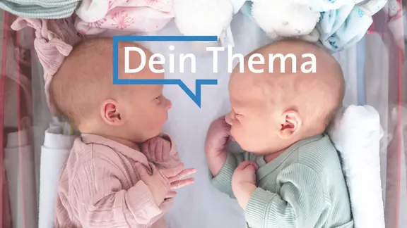 Zwei Babys liegen mit den Köpfen zueinander nebeneinander