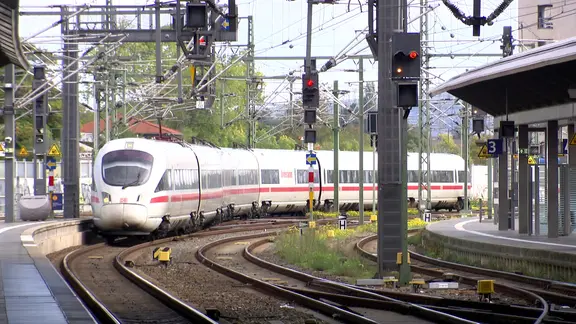 Ein ICE bei der Einfahrt in einen größeren Bahnhof; sonniges Wetter.