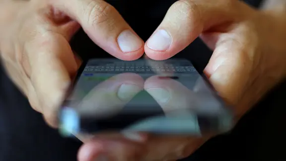 Ein Jugendlicher tippt auf einem Smartphone eine WhatsApp Nachricht.