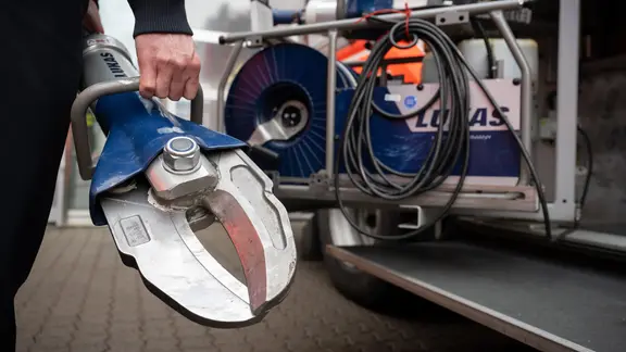 Ein Feuerwehrmann hält neben einem Fahrzeug eine hydraulische Schere in der Hand. 