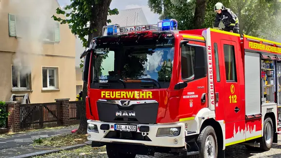 Ein Feuerwehrauto steht neben einem brennenden Haus.