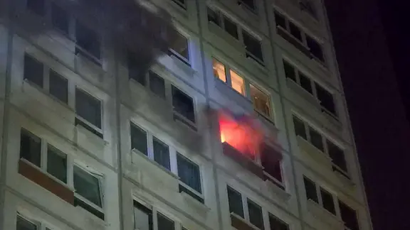 Aus einem Fenster in der zehnten Etage eines Wohnblocks in Leipzig dringen Flammen und Rauch.
