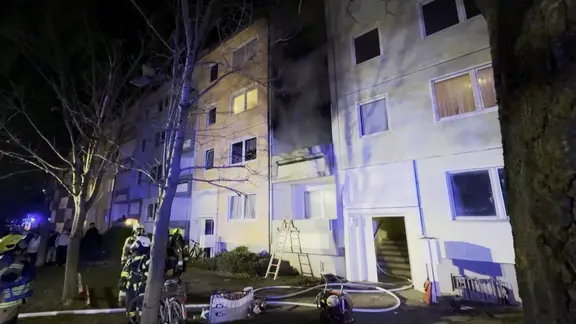 Feuerwehrleute mit Löschausrüstung an einem Neubauhaus, aus dem Rauch kommt