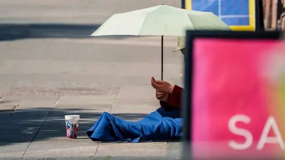 Eine Bettlerin schützt sich in der Innenstadt gegen die starke Sonne.
