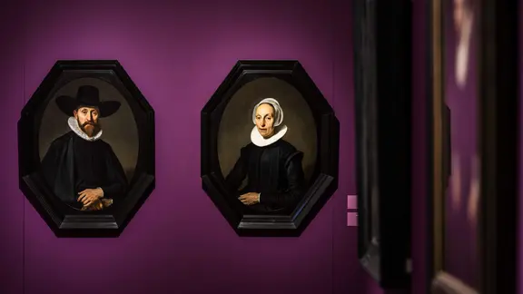 Zwei historische Gemälde hängen an einer lilafarbenen Wand in einer Ausstellung: Jacob Adriaensz. Backer: Bildnis eines Mannes und Bildnis einer Frau (1637), Privatsammlung