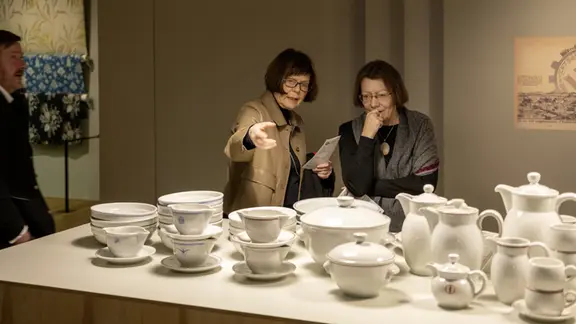 Zwei Frauen blicken und zeigen auf Geschirr in einer Ausstellung