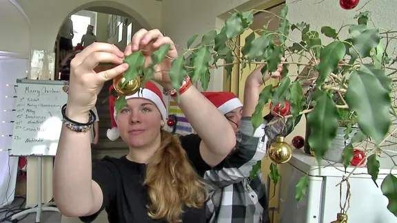 Eine Jugendliche im Landschulheim Neukirch schmückt einen Ficus mit Weihnachtskugel. 