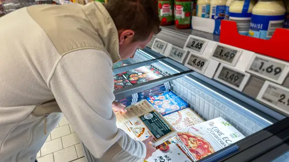 Mann betrachtet die Verpackung einer TK-Pizza