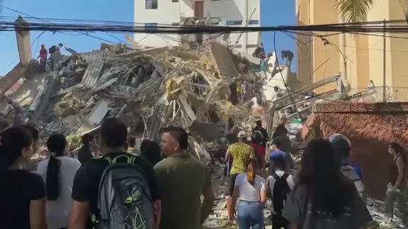 Nach einem Erdbeben in Kolumbien ist ein Gebäude eingestürzt. Viele Menschen stehen auf der Straße und blicken in Richtung der Trümmer. 
