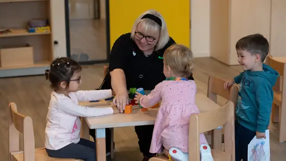 Kinder und eine Erzieherin spielen an einem Tisch.
