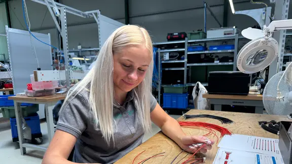 Eine junge Frau konfektioniert Kabel in einer Fertigungshalle.