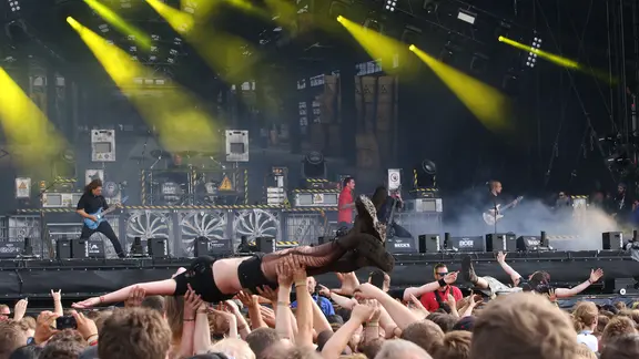 Eine Frau lässt sich bei einem Konzert über die Köpfe anderer Besucher hinweg heben