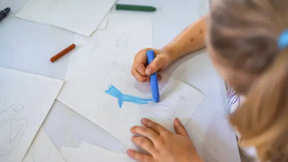 Ein Mädchen malt auf einem Stück Papier mit Wachsmalkreide