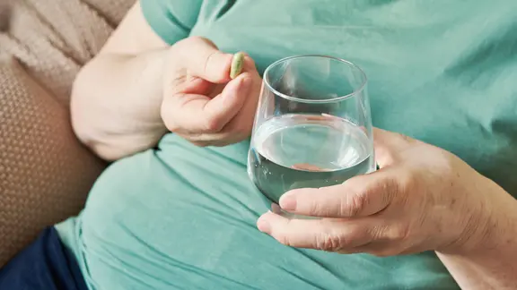 Ältere Frau mit Übergewicht nimmt täglich ein Nahrungsergänzungsmittel mit einem Glas Wasser ein Ältere Frau mit Übergewicht nimmt täglich ein Nahrungsergänzungsmittel mit einem Glas Wasser ein.