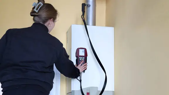 Eine Schornsteinfegerin überprüft eine Gastherme.