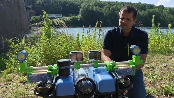Ein Wissenschaftler hockt neben einem Tauchroboter, der etwa so groß ist, wie ein großer Spielzeugbuggy. 