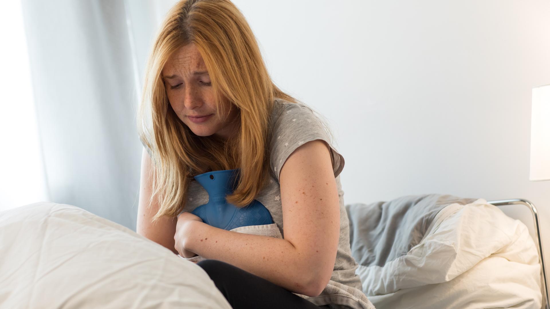 Eine junge Frau liegt im Bett und leidet unter Bauchkrämpfen | dpa-tmn | Christin Klose