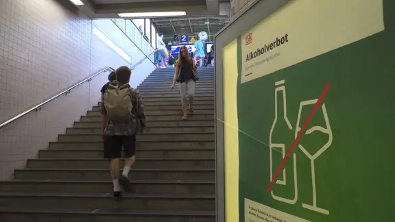 Ein Treppenaufgang zu einem Bahnsteig, links ein Aushang zum Alkoholverbot.