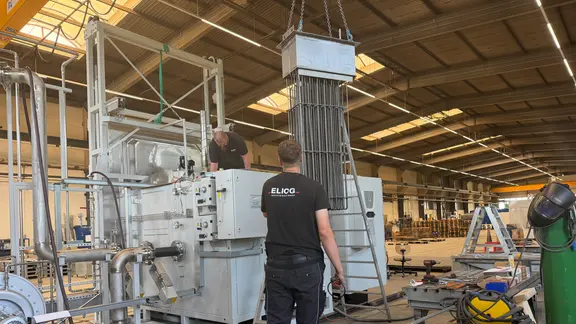 Zwei Männer in einer Fabrikhalle arbeiten an einem großen Gerät.