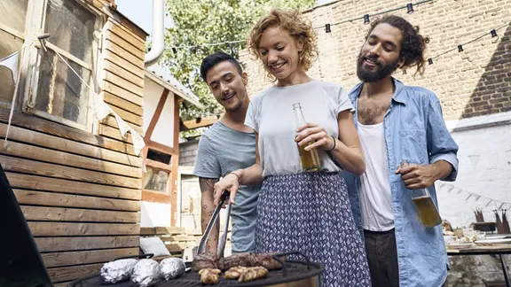 Freunde grillen im Garten und bereiten Fleisch auf einem Grill zu