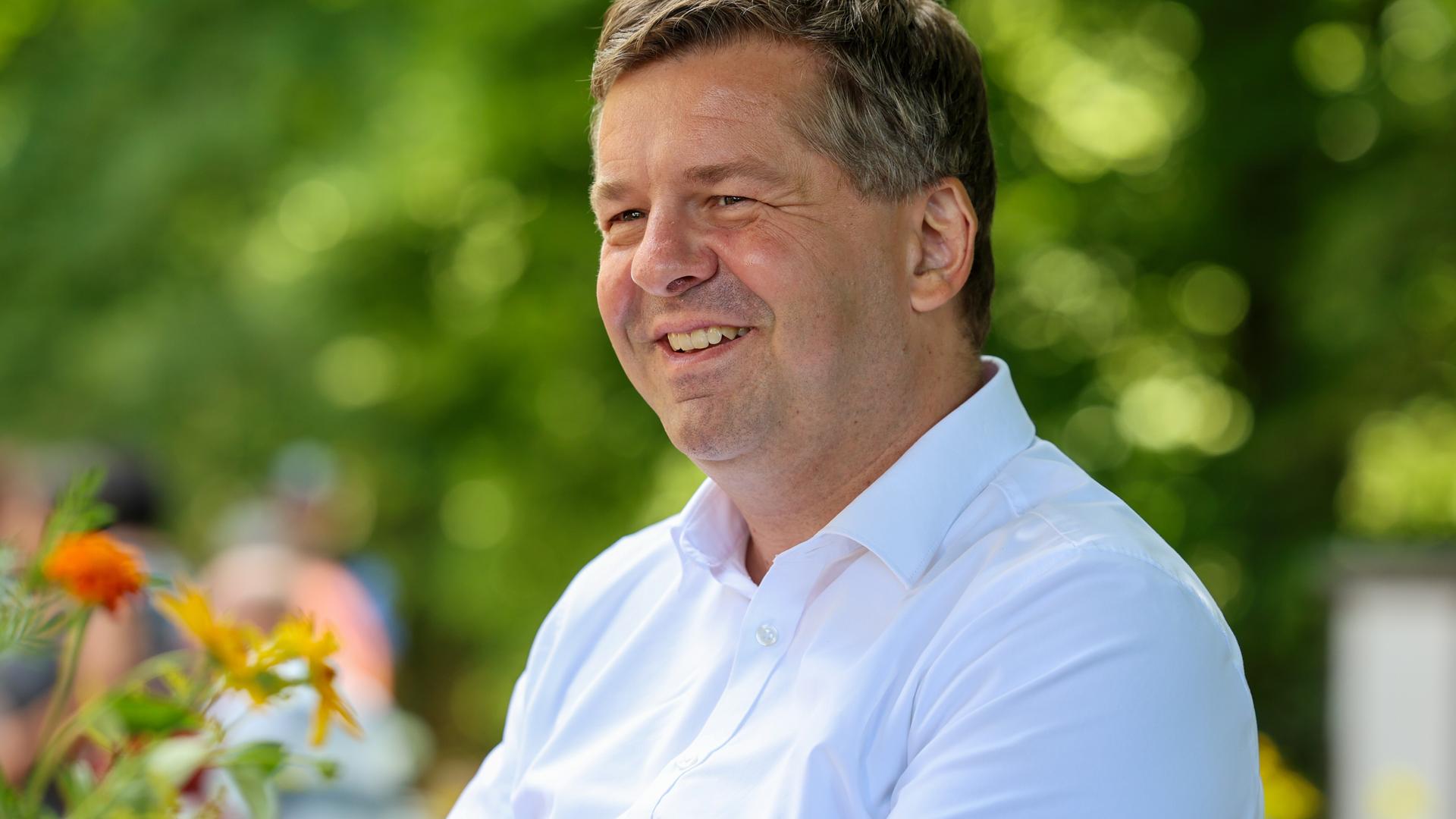 Porträt Sven Schulze in weißem Hemd mit Blumen im Hintergrund | picture alliance/dpa | Peter Gercke