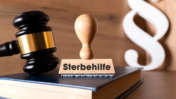 Ein Stempel mit der Aufschrift: Sterbehilfe, steht neben einem Richterhammer und einem Paragraphenzeichen.