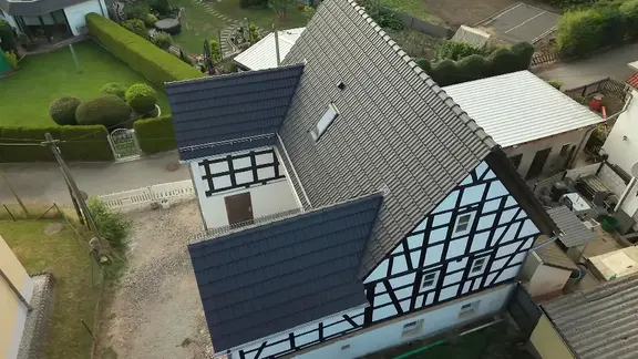 Luftaufnahme eines historischen Dreiseitenhofes, ein saniertes Fachwerkgebäude mit dunkelgrauem Ziegeldach.