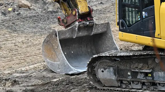 Ein Kettenbagger steht auf einer Baustelle zwischen Bauschutt und bewegt mit seiner Schaufel Trümmer. 