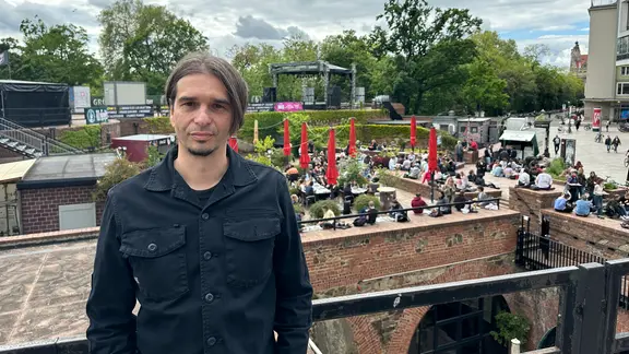 Ein Mann steht auf dem Dach der Moritzbastei. Er hat dunkle Kleidung an, schwarz-graue Haare und trägt einen Mittelscheitel. 