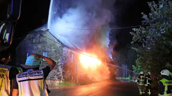 Feuerwehrleute stehen vor einem brennenden Bauernhaus
