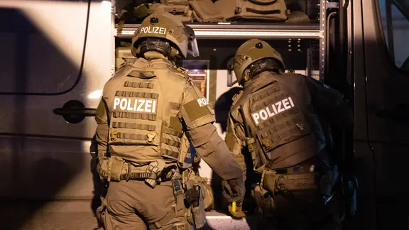 Zwei Personen in braunen Polizei-Uniformen mit Helmen vor einem geöffneten Transporter