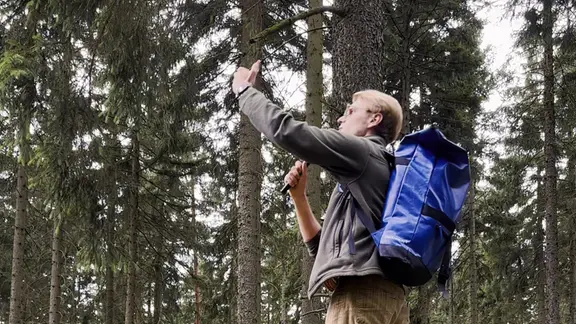 Ein Mann steht im Wald und hebt ein Telefon in die Luft.