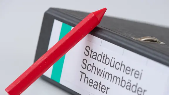 Ein roter Stift ist in Stuttgart neben einem Aktenordner mit der Aufschrift "Stadtbücherei, Schwimmbäder, Theater" zu sehen (Symbolfoto zum Thema "Kommunale Finanzen" vom 08.04.2010).
