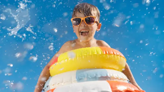 Happy child having fun on summer vacation. Funny kid jumping in swimming pool. Low angle view portrait of boy against water splash. Spring break!