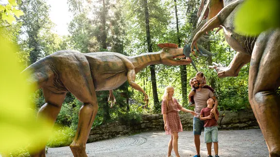 Eine Familie steht zwischen zwei großen Dinofiguren.