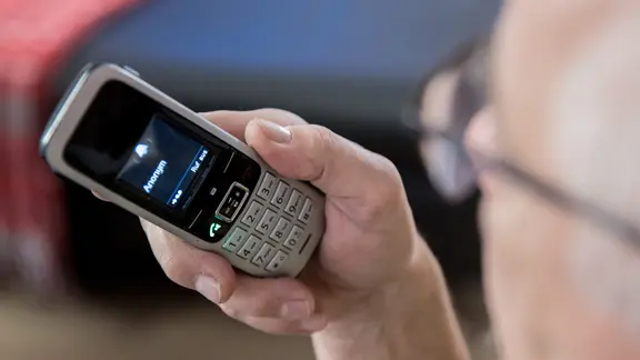 Ein älterer Mensch sitzt in seiner Wohnung und hält ein Telefon in der Hand.