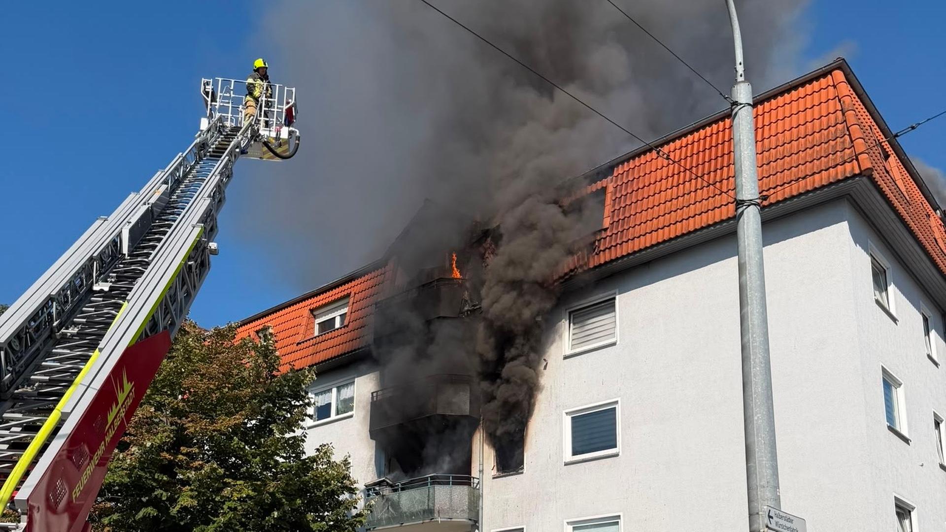 Aus einem Mehrfamilienhaus steigt dunkler Rauch auf. Vor dem Gebäude ein Feuerwehrmann auf einer Drehleiter.  | Feuerwehr Halberstadt