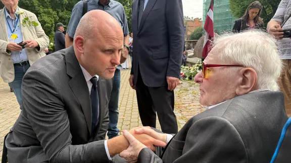 Ein alter Mann im Rollstuhl hät die Hände eines jüngeren Mannes, der vor ihm kniet.