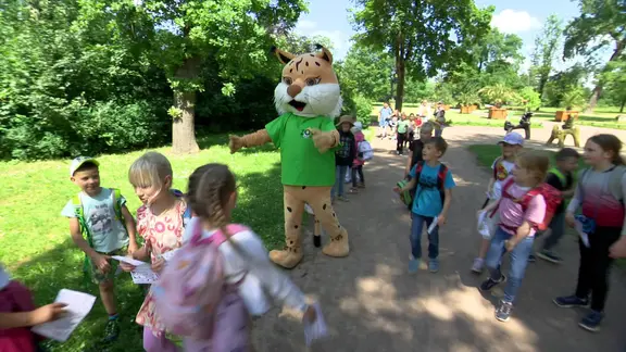 Viele Kinder laufen um eine Maskottchen herum.
