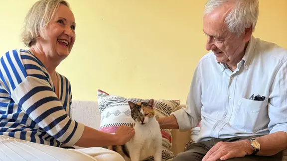 Ein Mann und eine Frau sitzen mit einer Katze auf einem Sofa.