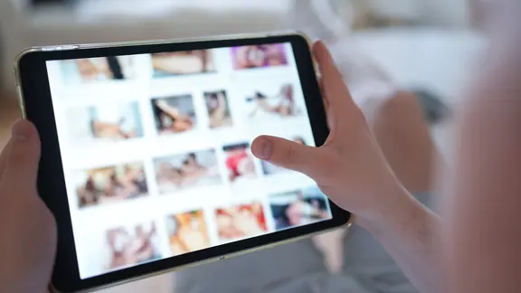 Ein junger Mann schaut sich auf einem Tablet eine Porno-Internetseite an